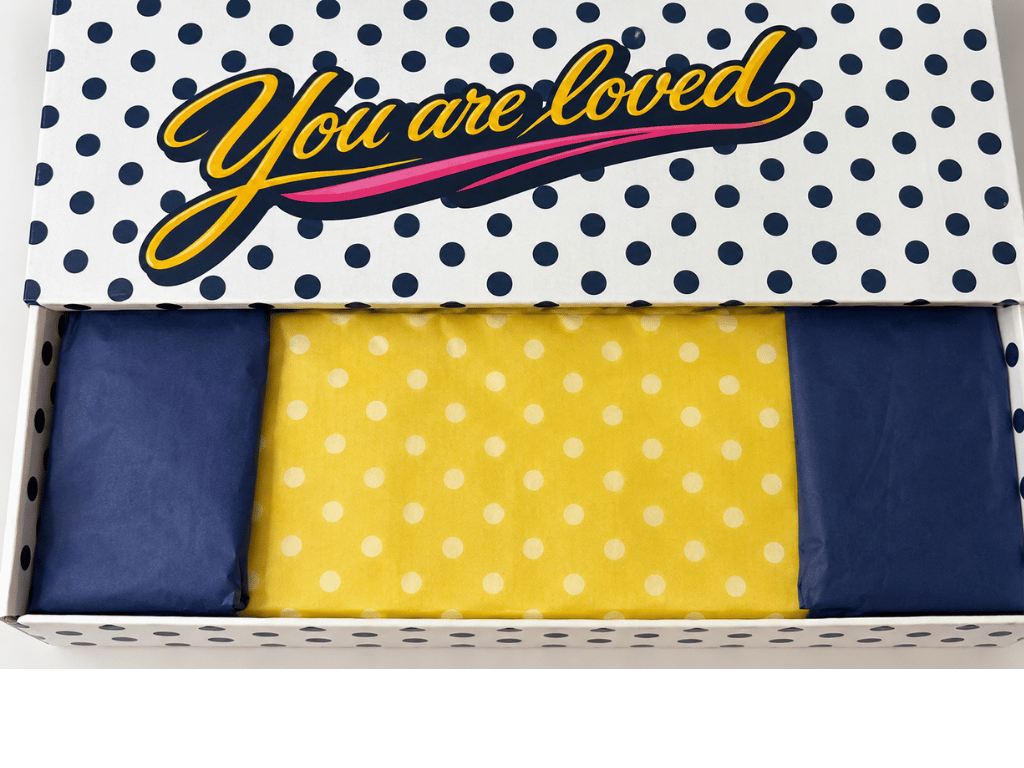 An InstaMom University box seen from above, lid reading 'You are loved', packed with navy and gold polka-dot tissue paper.